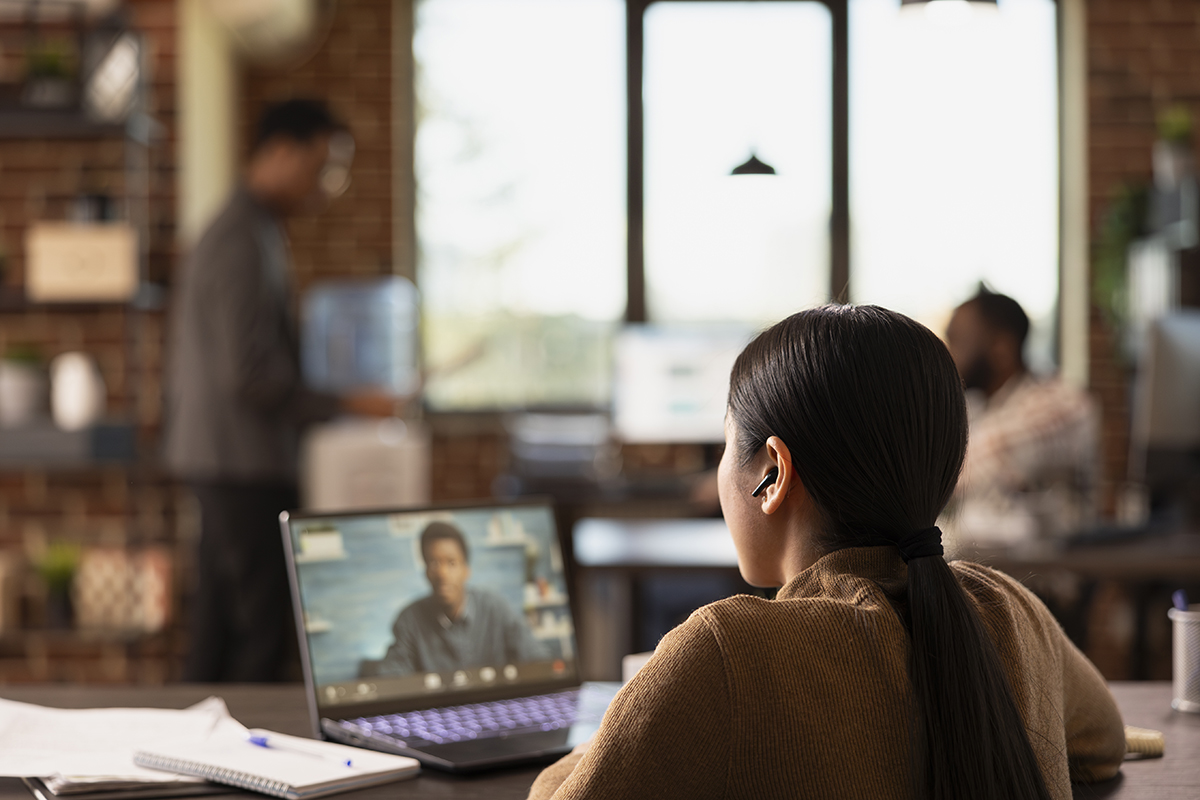 Businesswoman with wireless earphones, sitting at desk and having video call with african american coworker on laptop. Female entrepreneur on virtual meeting, having discussion with black male client.